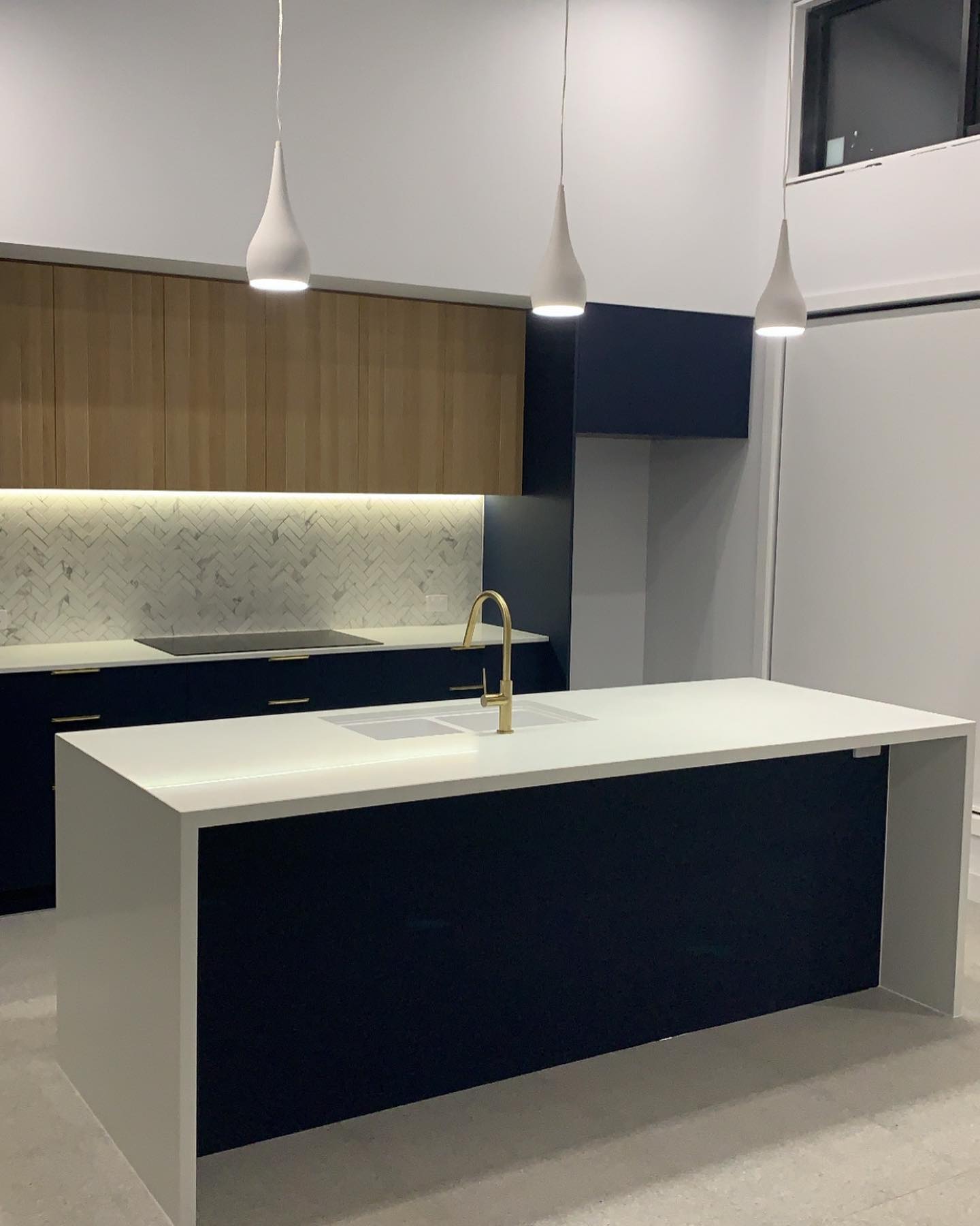 After: rebuilt Holt kitchen with navy cabinetry, timber accents and brass tapware