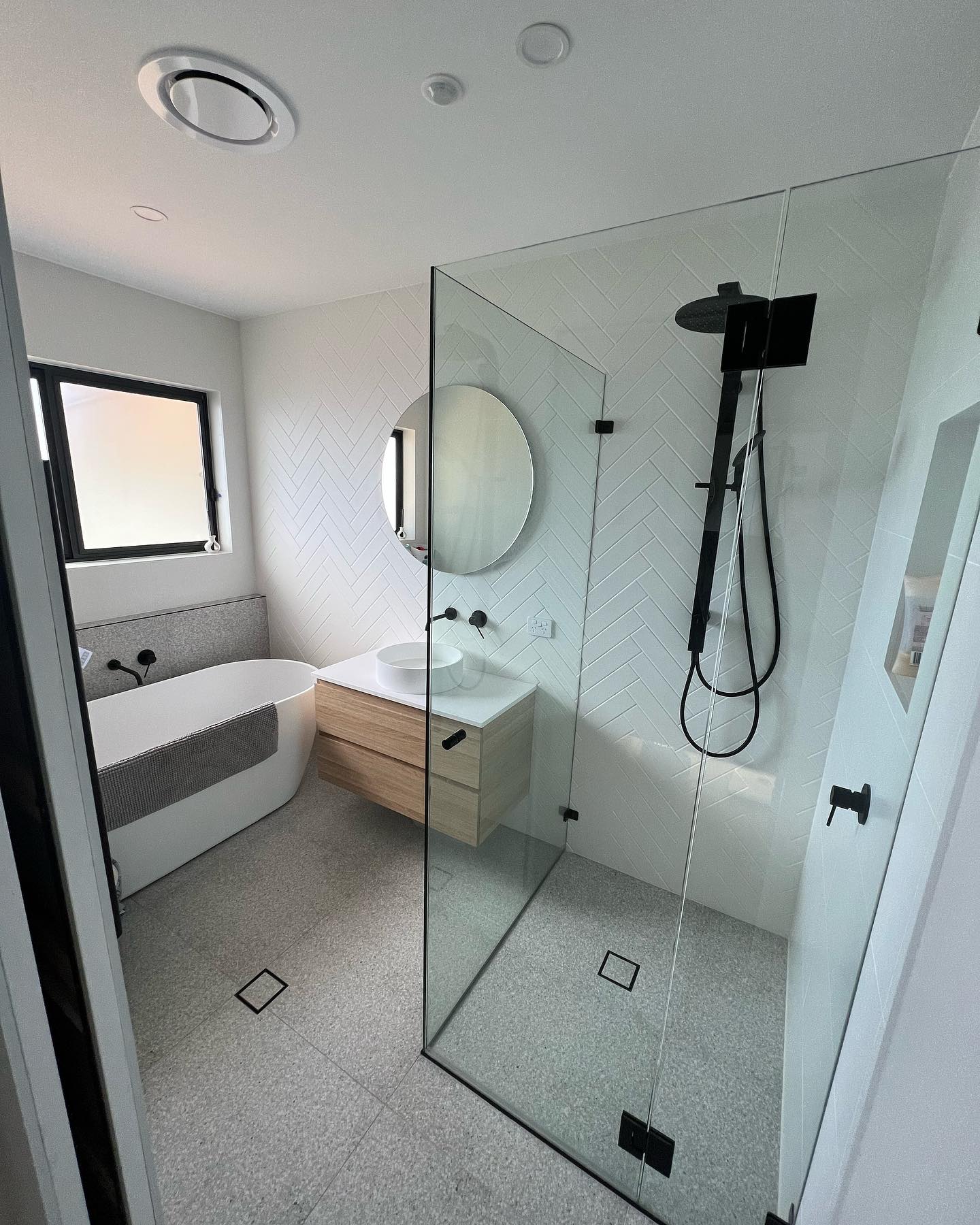 Renovated bathroom with herringbone tile, frameless glass shower, freestanding bath, floating timber vanity and matte black tapware, by BRT Building Canberra