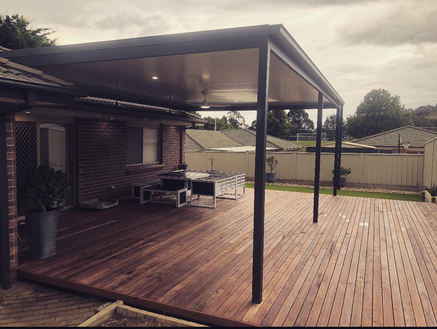 Hardwood deck under a charcoal-framed insulated-roof pergola attached to a brick home, by BRT Building Canberra
