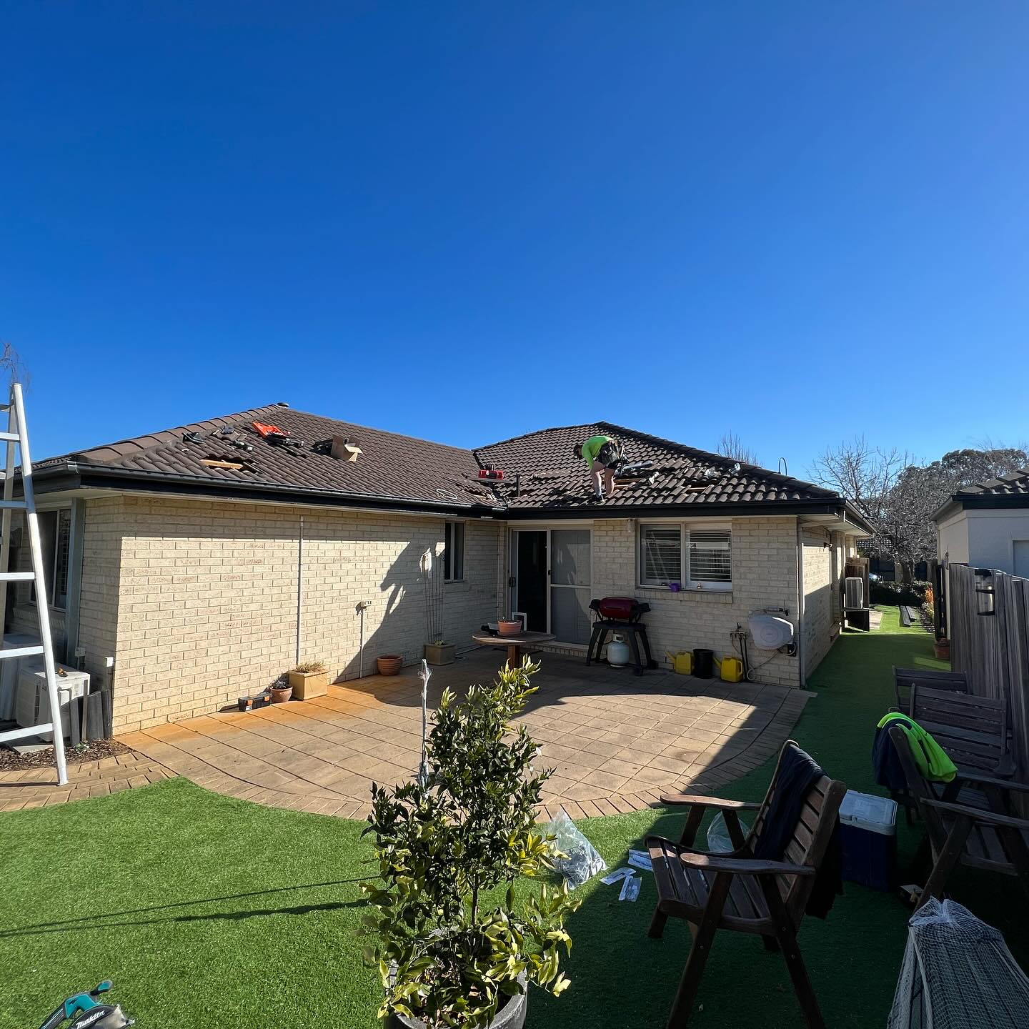 Tile roof repair in progress on a Canberra home, tradesperson on the roof replacing damaged tiles, by BRT Building