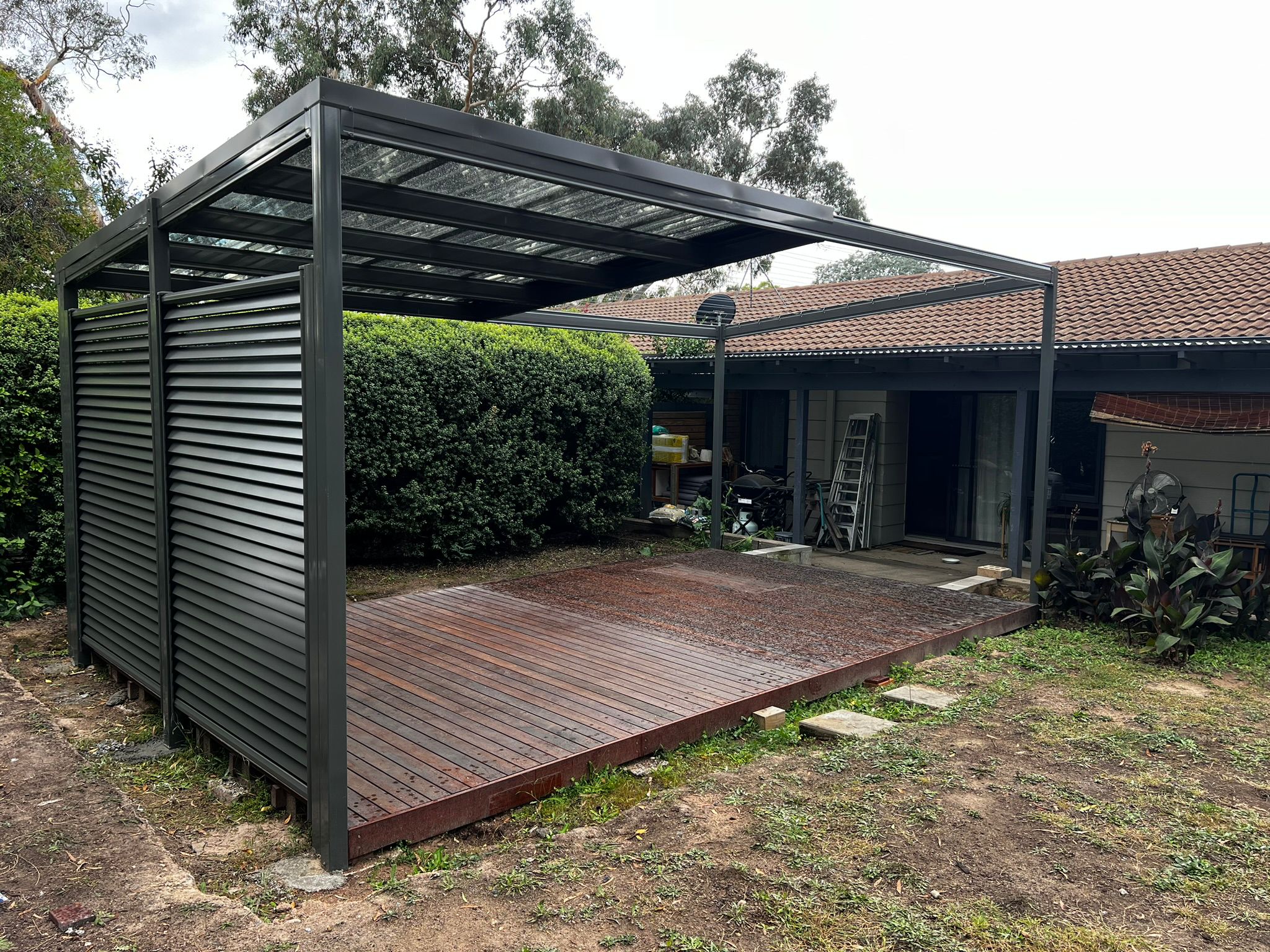 Matte black freestanding pergola with Laserlite roof and Louvrescreen privacy panels over hardwood deck, Torrens Canberra